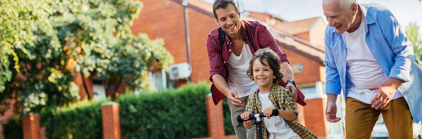 father and grandfather helping young boy learn to ride his bike